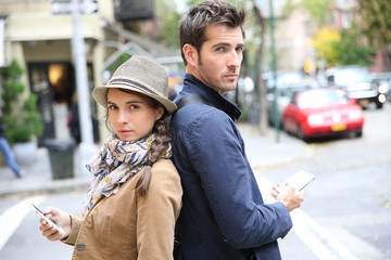 Couple standing back to back in street, using smartphone