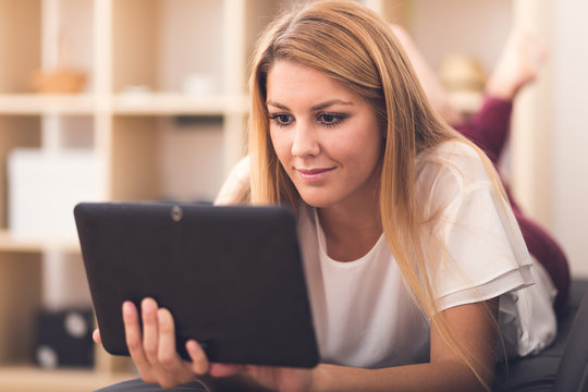 Smiling Young Woman Looking On Your Tablet Sitting On Sofa At Ho