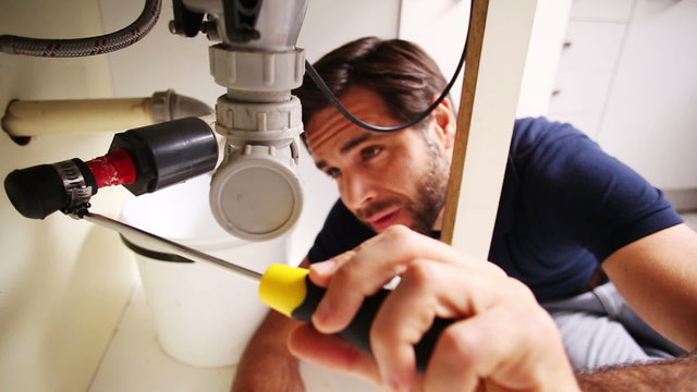 Handsome plumber using screwdriver to fix sink