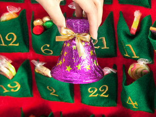 Mädchenhand hält eine Schokoladen-Weihnachtsglocke in violetter Verpackung aus dem Adventskalender