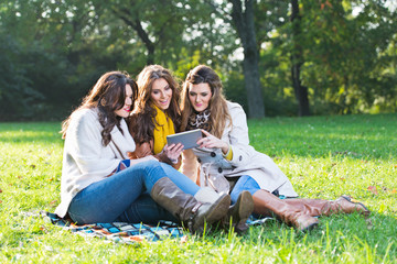 Three beautiful women using a tablet in the park