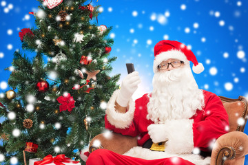 santa claus with smartphone and christmas tree