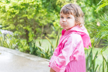 young child girl in raincoat under rain drops, outdoor portrait