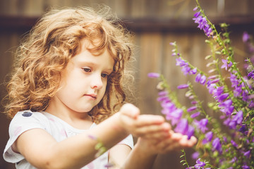 Naklejka premium Curly baby with flowers in her hand. Toning photo.