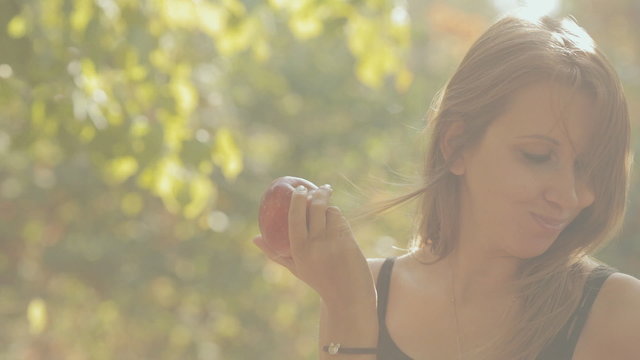 The girl eats a red apple in the forest
