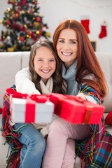 Fototapeta na wymiar Festive mother and daughter wrapped in blanket with gifts