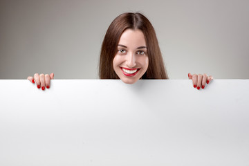 Woman showing white billboard over grey background in studio