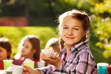 Smiling girl holds cupcake with her friends behind