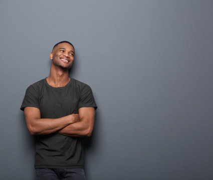 Cheerful young man smiling with arms crossed on gray background
