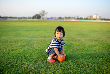 Asian girl playing ball in green field.