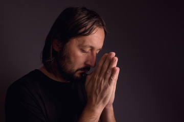 Adult bearded man praying in dark room