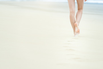 Slim girl in white swimsuit walking to ocean.