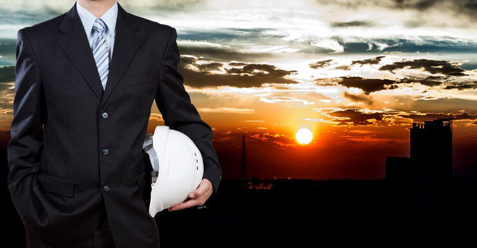Businessman holding safety helmet with city background