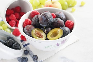 Seasonal fruits and berries in a white vintage bowl .