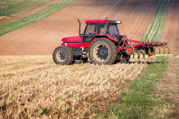 Red tractor harrowing a field. France