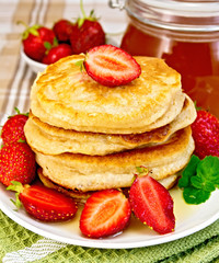 Flapjacks with strawberries and honey on tablecloth
