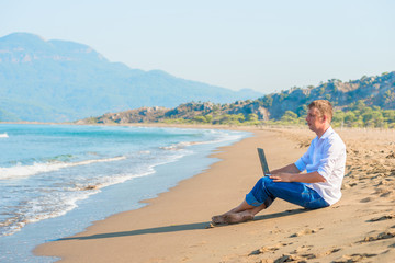 handsome young man with a laptop sitting on the beach