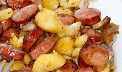 Plate of pieces of sausage, potatoes, garlic and meat with a pie
