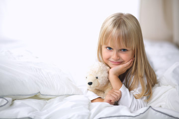 Little girl with teddy bear lying on the bed at home