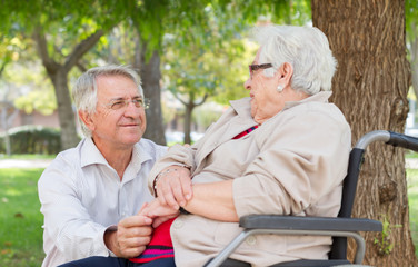 Man and senior woman in wheel chair talking at the park