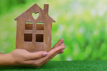 Woman hands holding small house on grass on bright background