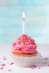 Delicious birthday cupcake on table on light blue background