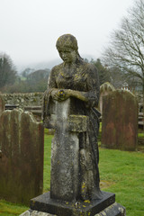 Lady leaning on cross tombstone looking over grave in cemetery