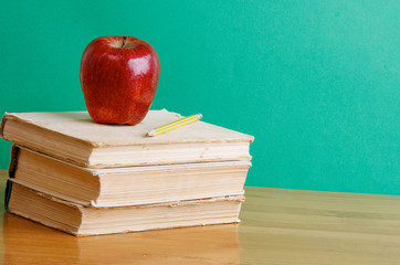 A pencil and a red apple on a pile of books
