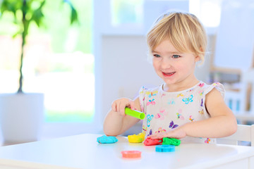 Cute toddler girl playing with dough, colorful modeling compound