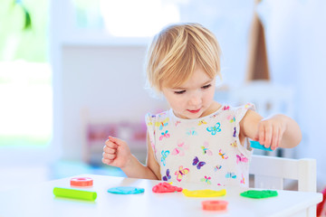 Cute toddler girl playing with dough, colorful modeling compound