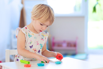 Cute toddler girl playing with dough, colorful modeling compound