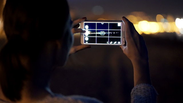 Woman talking photo of city lights with cellphone at night