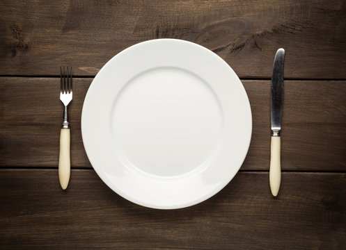empty plate on a wooden table with fork and knife