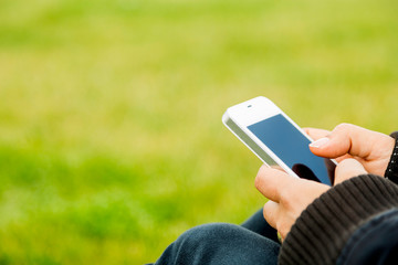 Young woman sitting on grass and using smart phone close-up