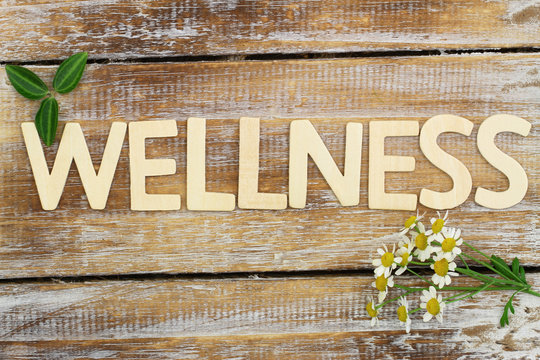 Wellness written with wooden letters, chamomile flowers on wood