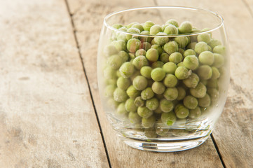 glass of frozen peas on wooden background