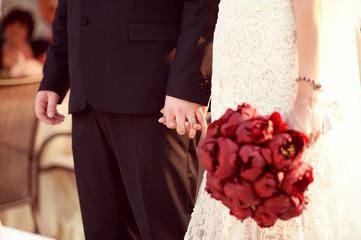 beautiful bride and groom holding red flowers bouquet in hands