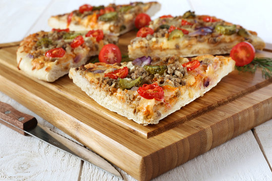 Four pieces of tasty pizza with tomatoes, pickles and minced mea