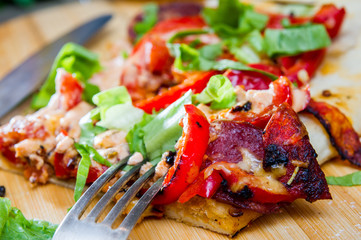 slice of pizza with peppers, bacon and herbs on a wooden board