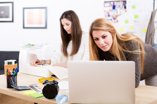Young attractive females fashion designers leaning on office des