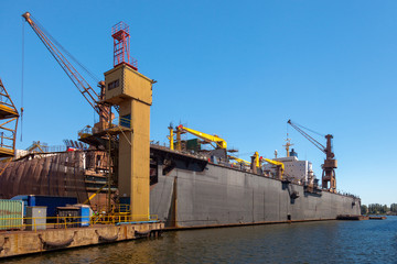 Dry floating dock and cranes in shipyard.