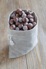 Hazelnuts in a burlap bag on a wooden table.