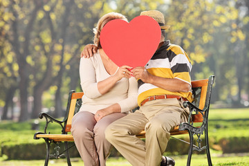 Mature couple kissing behind a red heart in a park