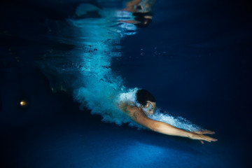 Man with splash swimming under dark blue water