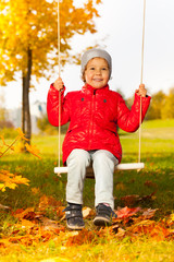 Happy girl sits on swings and smiles cheerfully