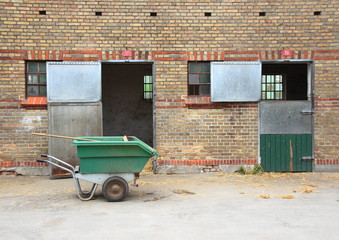 Empty horse stables with dirt wagon on asphalt