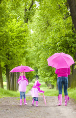 mother and her daughters with umbrellas in spring alley