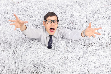 Terrified man drowning in a pile of shredded paper