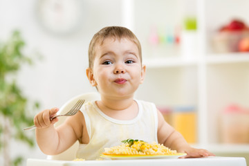 cute kid boy in a highchair for feeding with a fork and a pasta