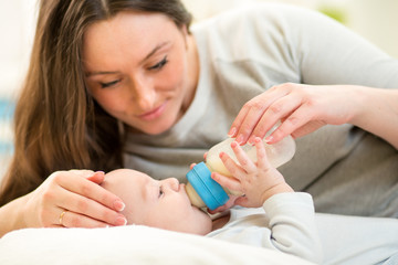 Obraz na płótnie Canvas mother at home feeding baby boy with a milk bottle